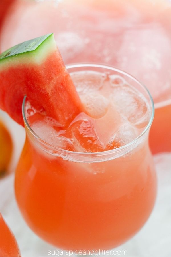 close-up image of a mini-hurricane glass filled with ice and watermelon lemonade garnished with a wedge of watermelon