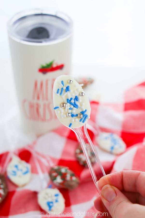 a hand holds up a white chocolate Christmas spoon with more chocolate spoons and a Christmas mug of coffee in the background