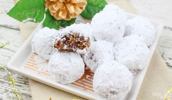 powdered sugar coated rum balls on a white plate garnished with Christmas decorations