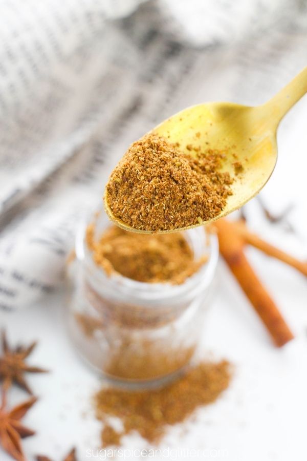 gold spoon holding a scoop of Chinese Five Spice with a jar full in the background
