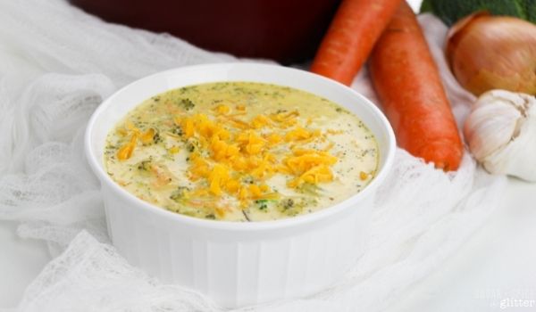 a white bowl of broccoli cheddar soup along with the ingredients needed to make the soup in the background
