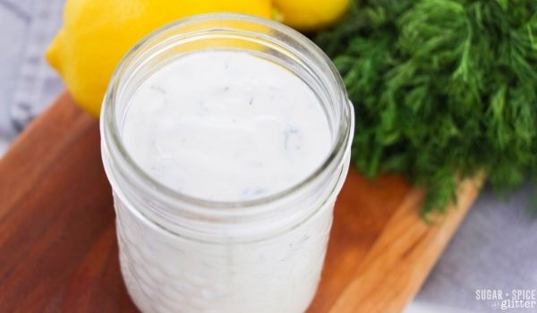 a mason jar of creamy lemon dill salad dressing along with a bundle of dill and a lemon in the background