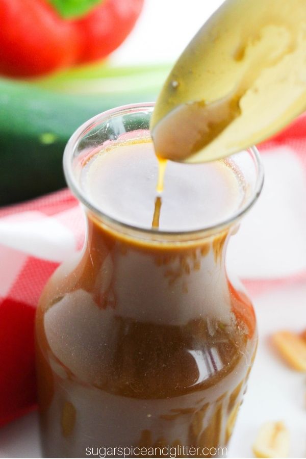 a golden spoon pours some Kung Pao Sauce into a glass jar holding more sauce in front of a red plaid napkin