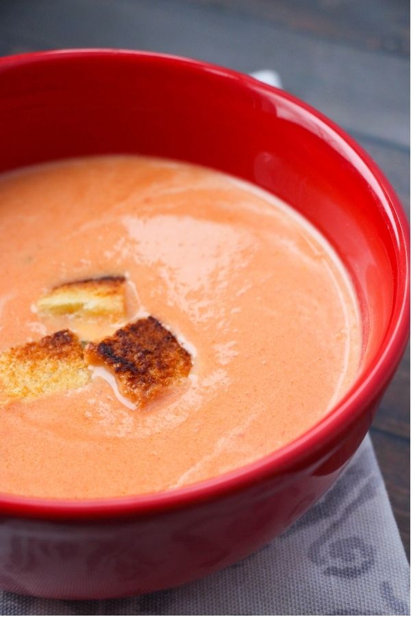close-up picture of a red bowl filled with creamy tomato soup with a few grilled cheese croutons sprinkled on top