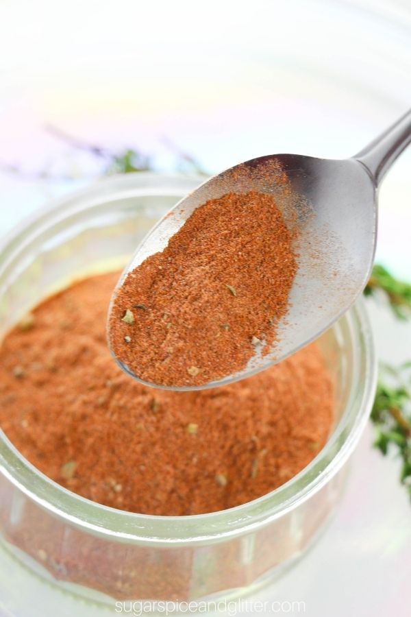 a spoon holding some blackening spice overtop of a jar holding more seasoning