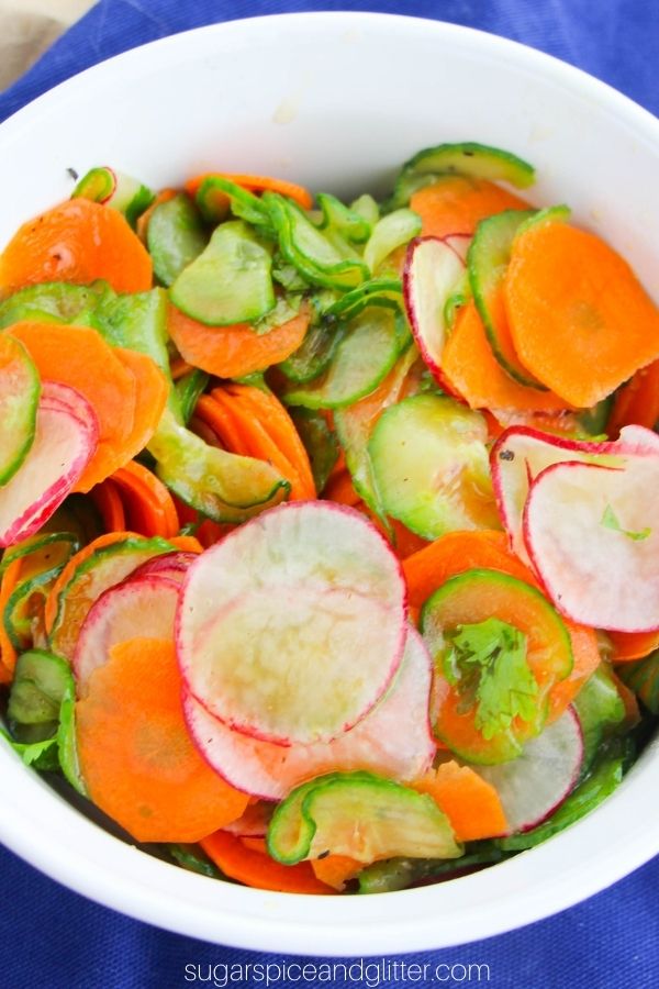 overhead shot of a white bowl filled with thinly sliced carrots, cucumber and radishes dressed with a cilantro-lime dressing