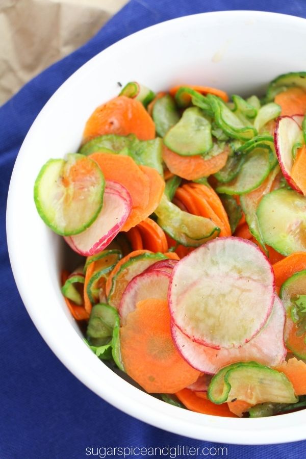 overhead shot of a white bowl filled with thinly sliced carrots, cucumber and radishes dressed with a cilantro-lime dressing