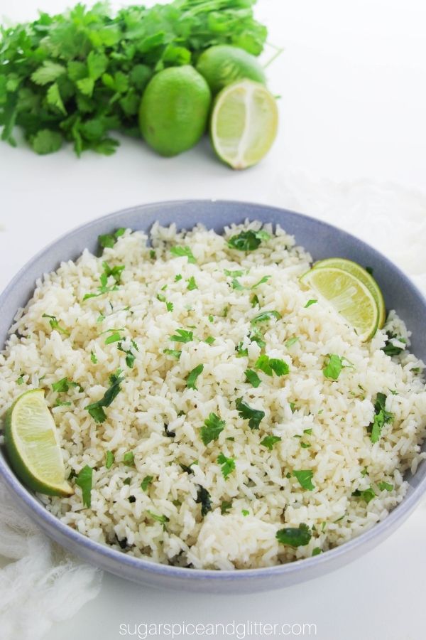 light blue bowl filled with cilantro lime rice, garnished with lime wedges with ingredients needed to make the recipe in the background
