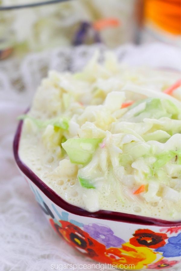 close-up image of a floral bowl filled with coleslaw on a white muslin napkin