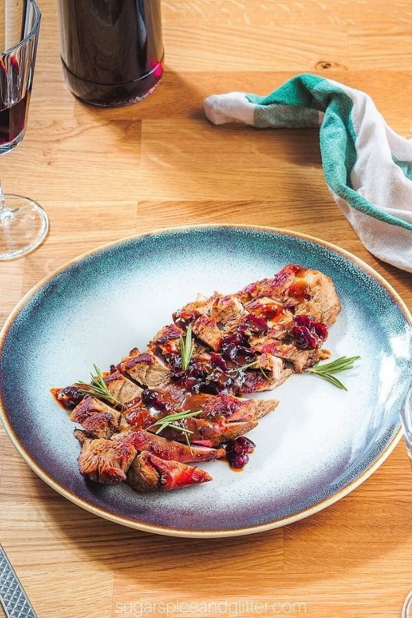 cranberry orange pork tenderloin on a blue platter on a table with red wine in the background