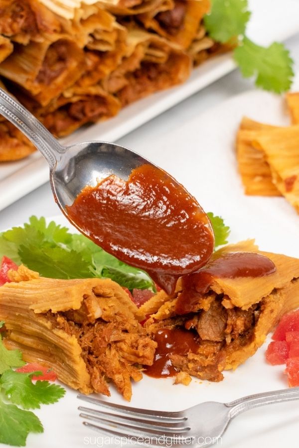 a cut-in-half pork tamal having chili sauce spooned overtop of it