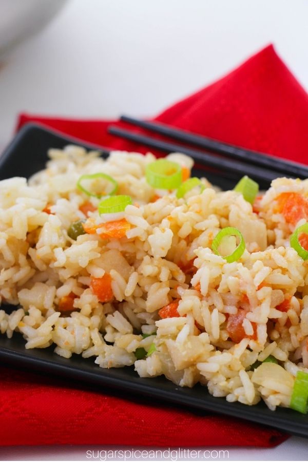 black square dish piled high with fried rice on a red napkin with black chopsticks in the background