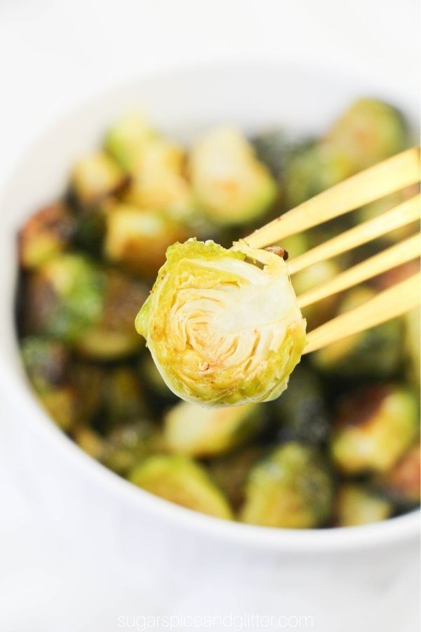 a roasted Brussels sprout on a fork overtop of a dish full of more roasted sprouts