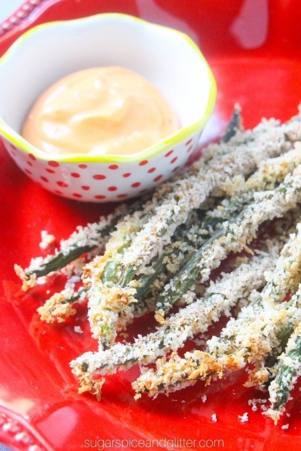 green bean fries on a red plate alongside a spicy aioli dip