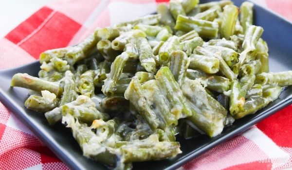 close-up image of cheesy green beans on a black, square plate