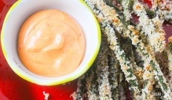 overhead image of green bean fries on a red plate with a red dip