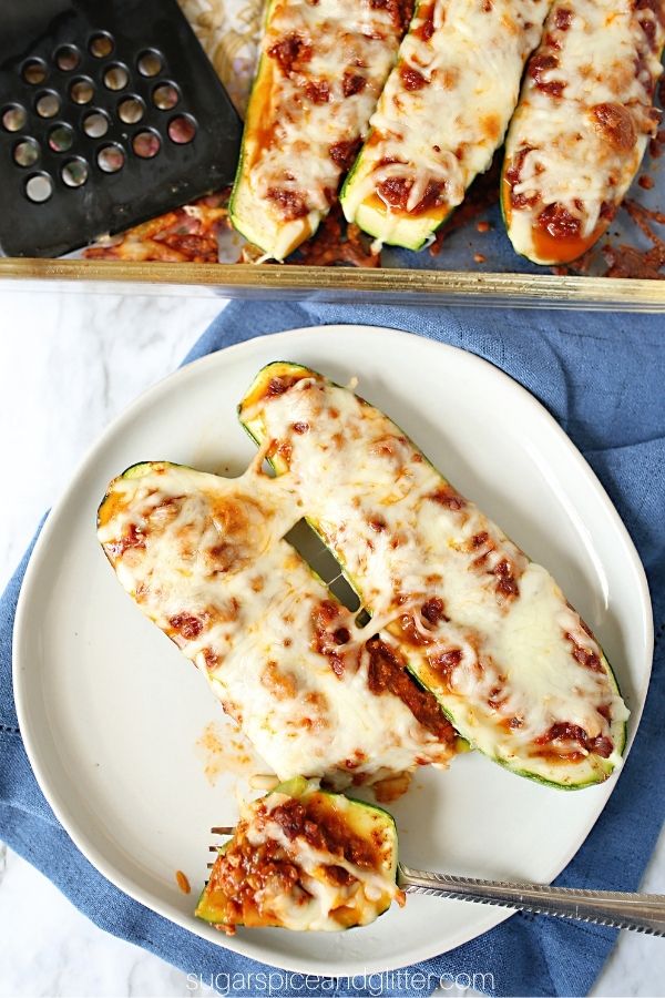 a fork holding a bite of a taco-stuffed zucchini boat on a white plate with 2 zucchini boats set on a denim napkin