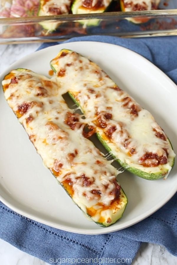 a white plate of two Taco-Stuffed Zucchini Boats, with a glass casserole dish holding more zucchini boats in the background