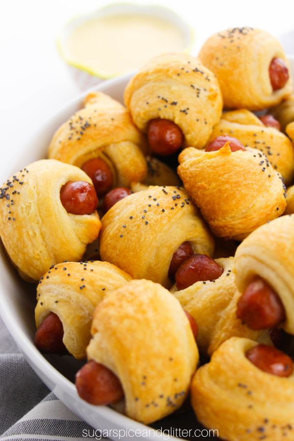 close-up image of a bowl full of piggies in a blanket with dipping sauce in the background