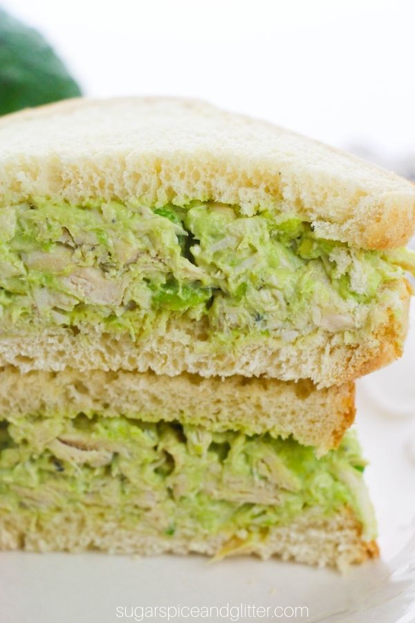 close-up of a stack of sliced avocado chicken salad sandwiches on a white plate