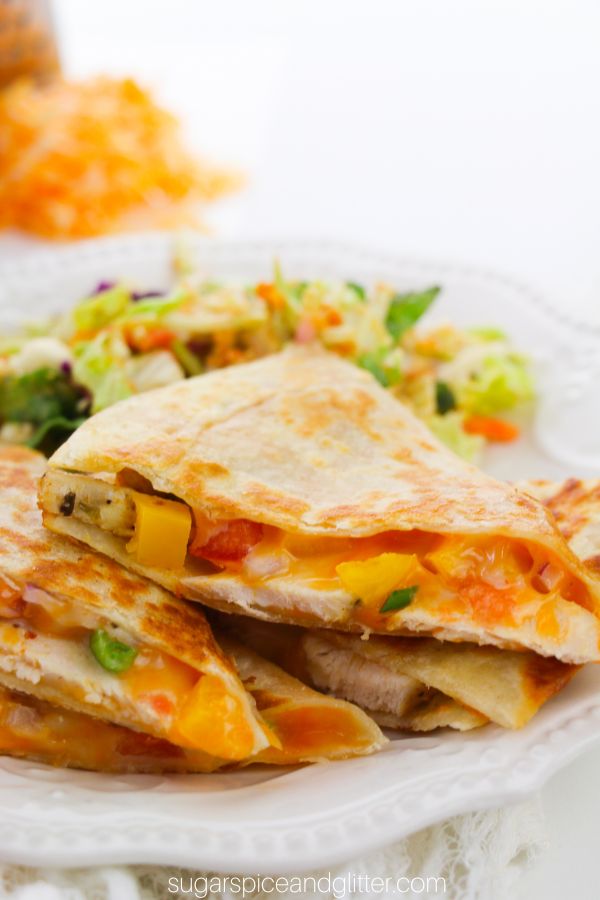 close-up image of a chicken quesadilla with veggies and melted cheese peeking out on a white plate with a side salad