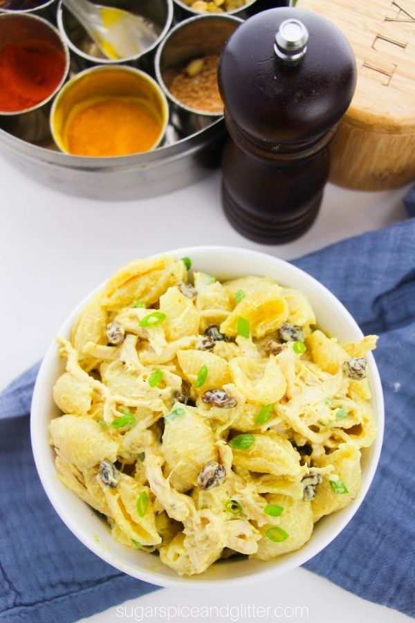 a white bowl filled with Bombay chicken pasta salad set on a blue napkin with Indian spices in the background