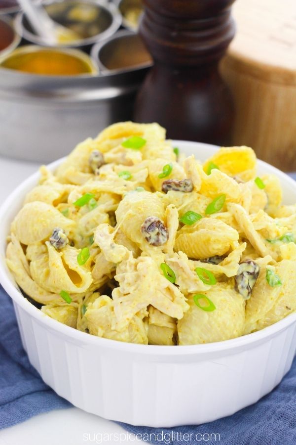 a white bowl filled with Bombay chicken pasta salad set on a blue napkin with Indian spices in the background
