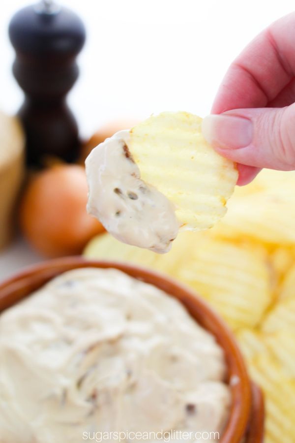 hand holding a chip loaded with French onion dip with pepper, onions and salt in the background