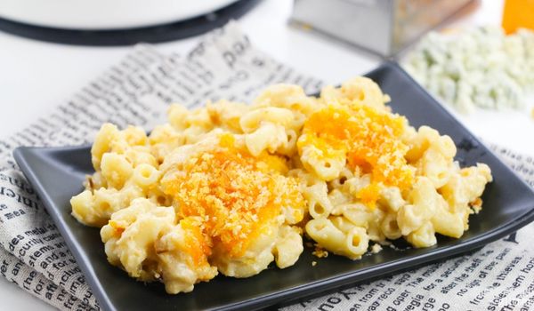 blue cheese mac and cheese on top of a square black plate set on a newsprint napkin with ingredients needed to make the recipe in the background