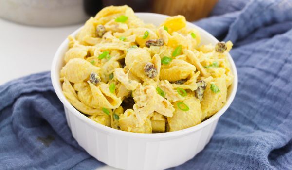 a white bowl filled with Bombay chicken pasta salad set on a blue napkin