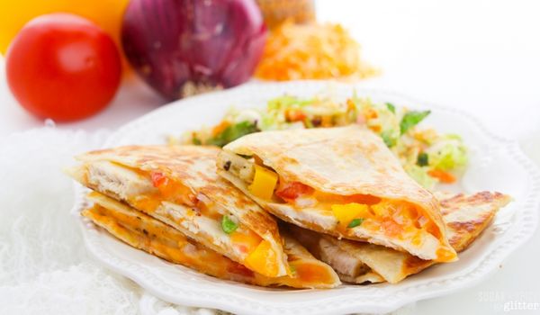 white plate filled with chicken quesadillas and a side salad, with ingredients to make a chicken quesadilla in the background