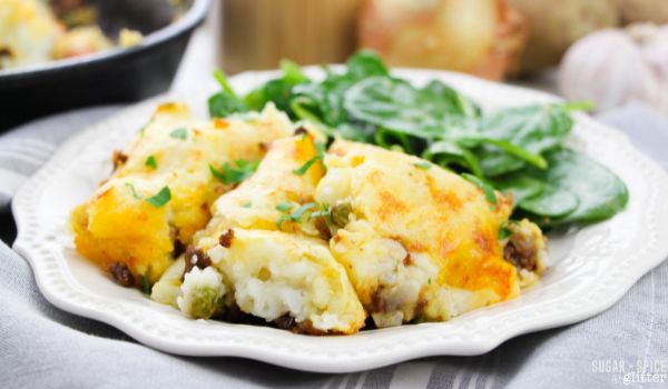 a white plate with a generous helping of cottage pie served alongside a simple spinach salad