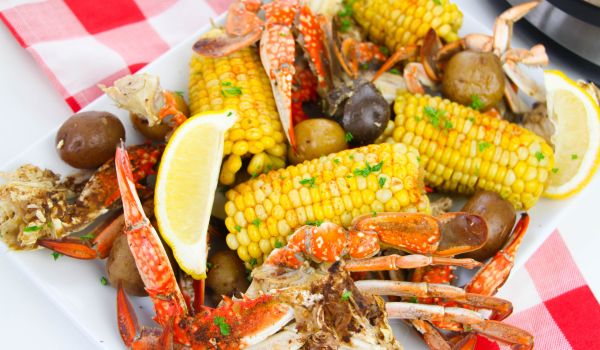 a white platter holding a seafood boil consisting of crab legs, corn and potatoes, garnished with lemon wedges