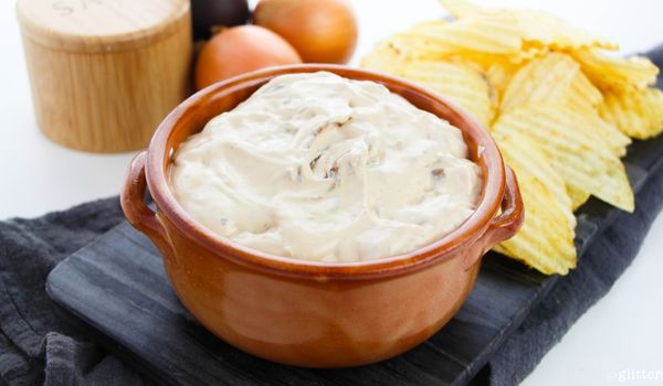 picture of French Onion dip in a terra cotta bowl with pepper, salt, onions and chips in the background