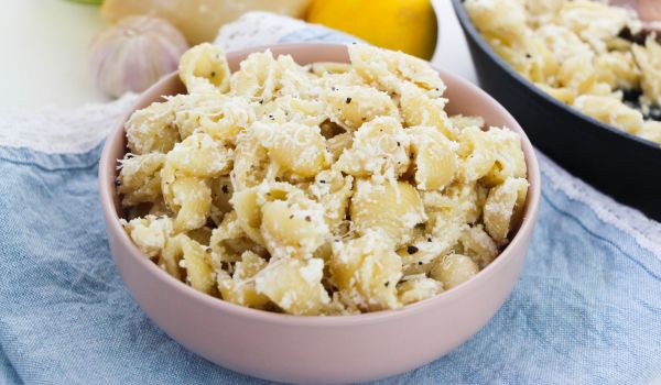 a pink bowl filled with creamy Lemon Ricotta pasta set on a denim napkin with a cast-iron pan holding more of the pasta in the background