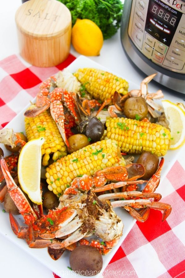 a white platter holding a seafood boil consisting of crab legs, corn and potatoes, garnished with lemon wedges set in front of an Instant Pot