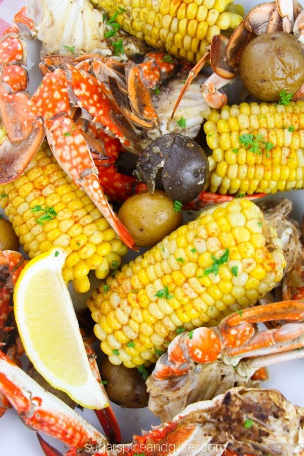 close-up image of a seafood boil consisting of crab legs, corn and potatoes, garnished with lemon wedges