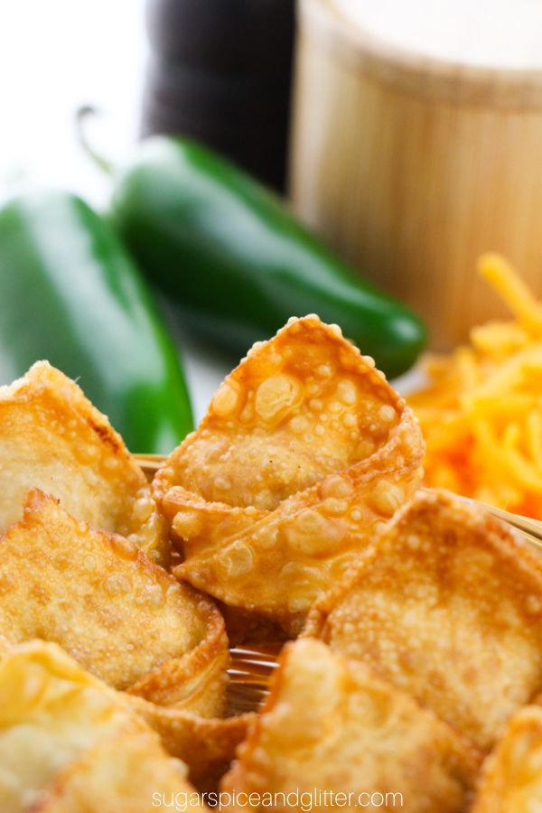 close-up picture of jalapeno popper wontons in a wicker basket with jalapenos, cheddar cheese and seasonings in the background
