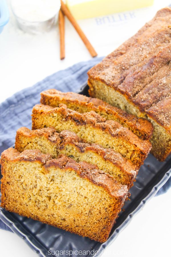 sliced snickerdoodle banana bread on a navy blue platter with ingredients needed to make the recipe in the background