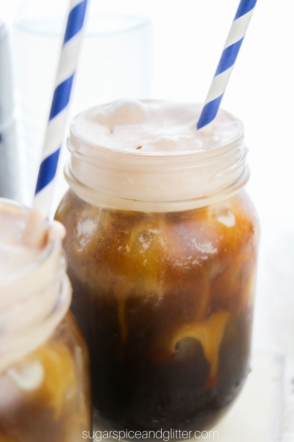 a close-up picture of a mason jar filled with chocolate cold brew coffee topped with chocolate cold foam, with a blue striped paper straw inserted