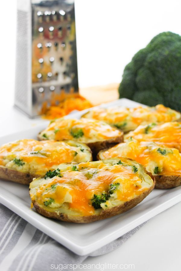 cheesy twice baked potatoes with bits of steamed broccoli peeking out from under the cheese, set on a white plate, with cheese and broccoli in the background