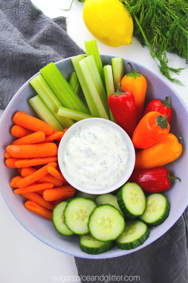 overhead image of a large blue bowl filled with fresh veggies, in the center is a white bowl filled with dill dip