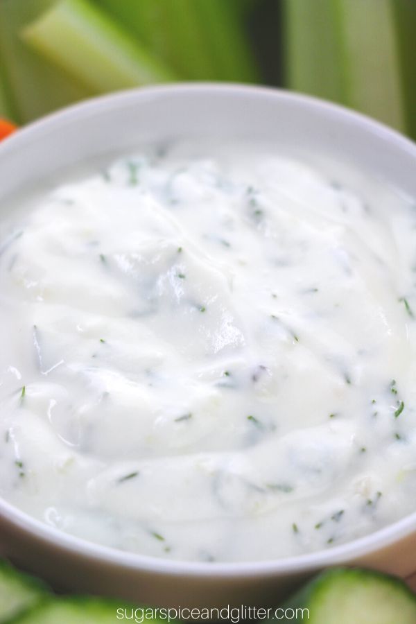 close-up image of a beige bowl holding dill veggie dip, surrounded by sliced veggies