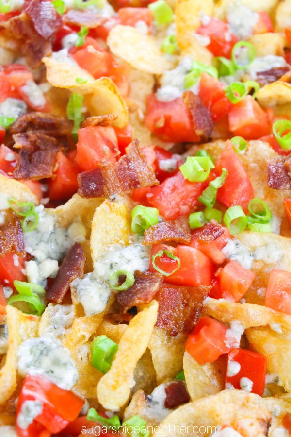 close-up image of kettle chips topped with melted blue cheese, tomatoes, bacon and green onions