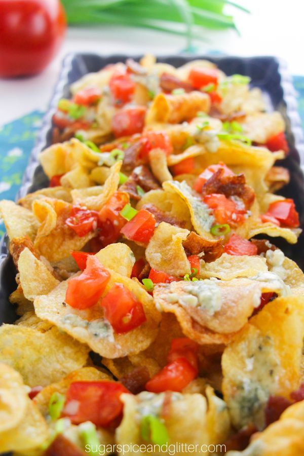 close-up image of kettle chips on a blue platter topped with melted blue cheese, tomatoes, bacon and green onions