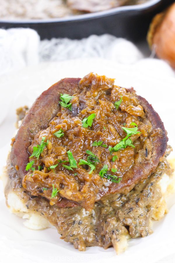 a steak smothered in onion gravy and sprinkled with parsley on a white plate