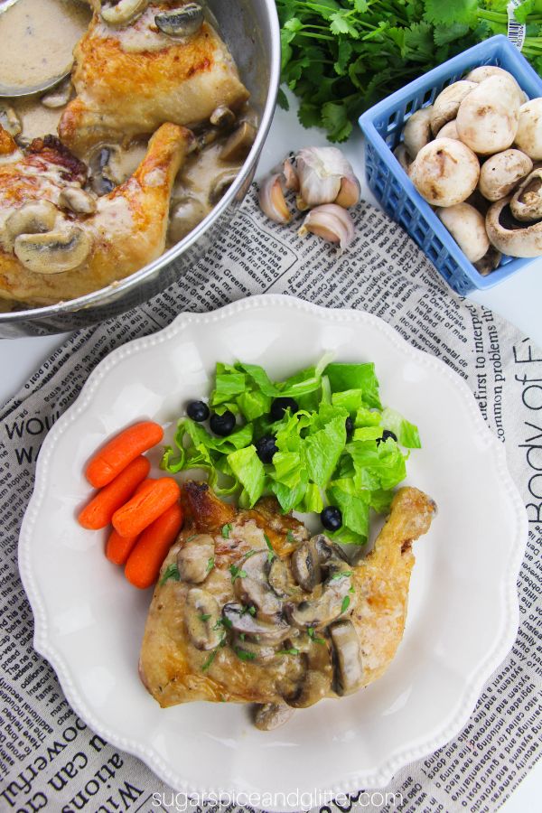 overhead image of browned chicken quarters smothered with creamy mushroom sauce on a white plate with a side salad and cooked carrots along with a pan of more chicken and mushroom sauce in the background