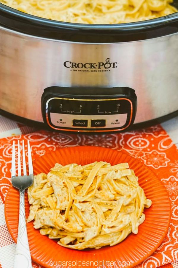 red plate full of cajun chicken pasta in front of a crockpot