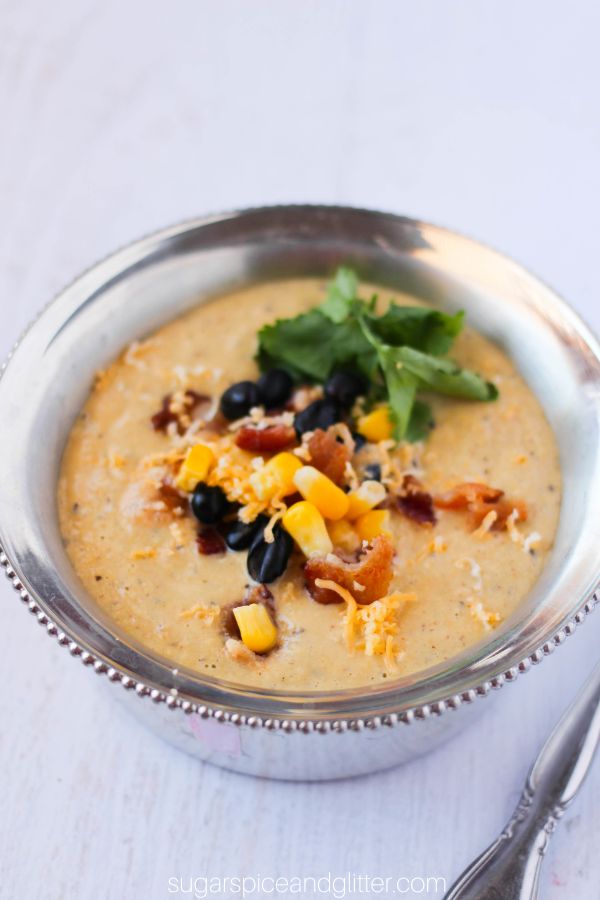 overhead image of corn chowder in a silver bowl with corn, black beans, bacon, cilantro and cheese sprinkled on top