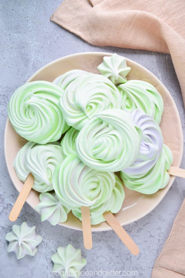 overhead image of green and lavendar-swirled meringue cookie pops in a beige bowl